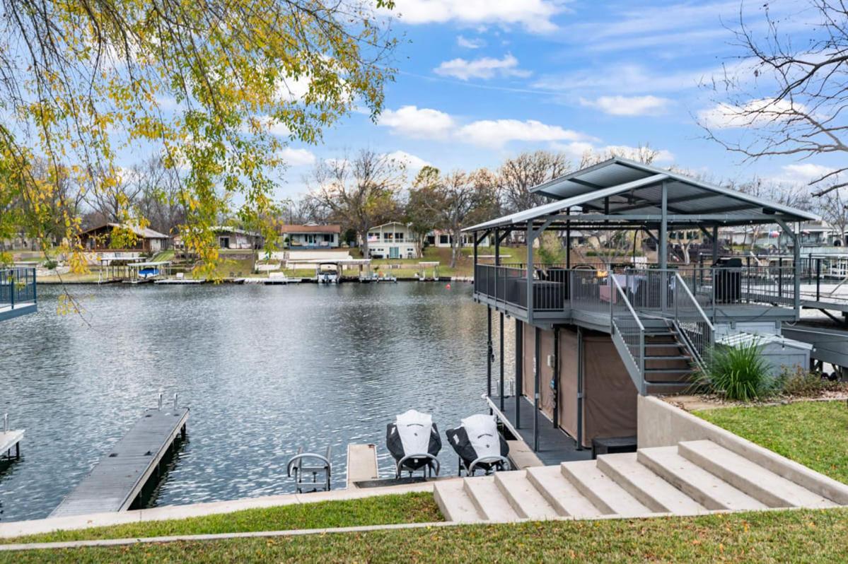 A Lakeside scene at LUBINBERRY features a covered two-level dock, jet skis, and a boat slip. Steps and grass lead to the water, with houses and trees across the lake beneath a partly cloudy sky.