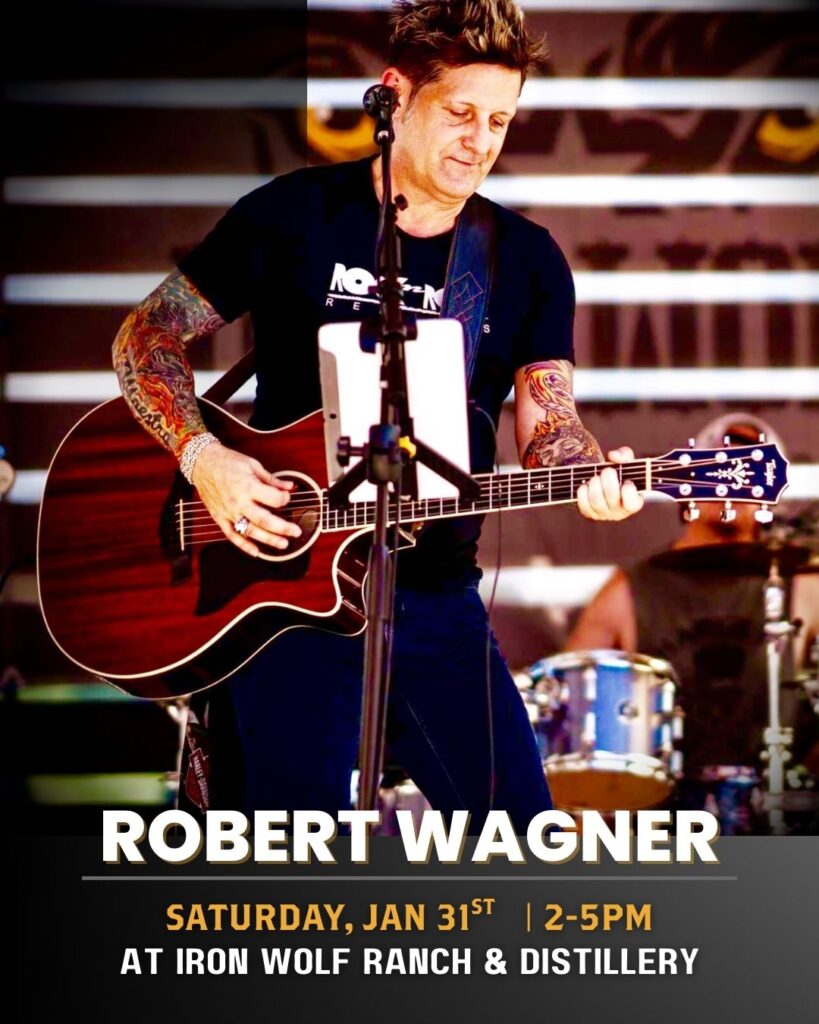 A tattooed musician plays an acoustic guitar and sings on stage. Text reads: Robert Wagner, Saturday, Jan 31st | 2-5pm at Iron Wolf Ranch & Distillery. A drummer is visible in the background.