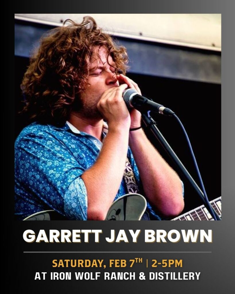 A man with curly hair sings passionately into a microphone while playing guitar. Text below reads: Garrett Jay Brown. Saturday, Feb 7th | 2-5pm at Iron Wolf Ranch & Distillery.