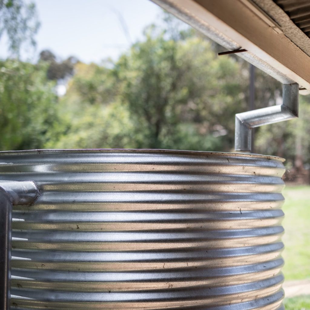 Galvanized rainwater collection tank connected to corrugated roof in rural Central Texas